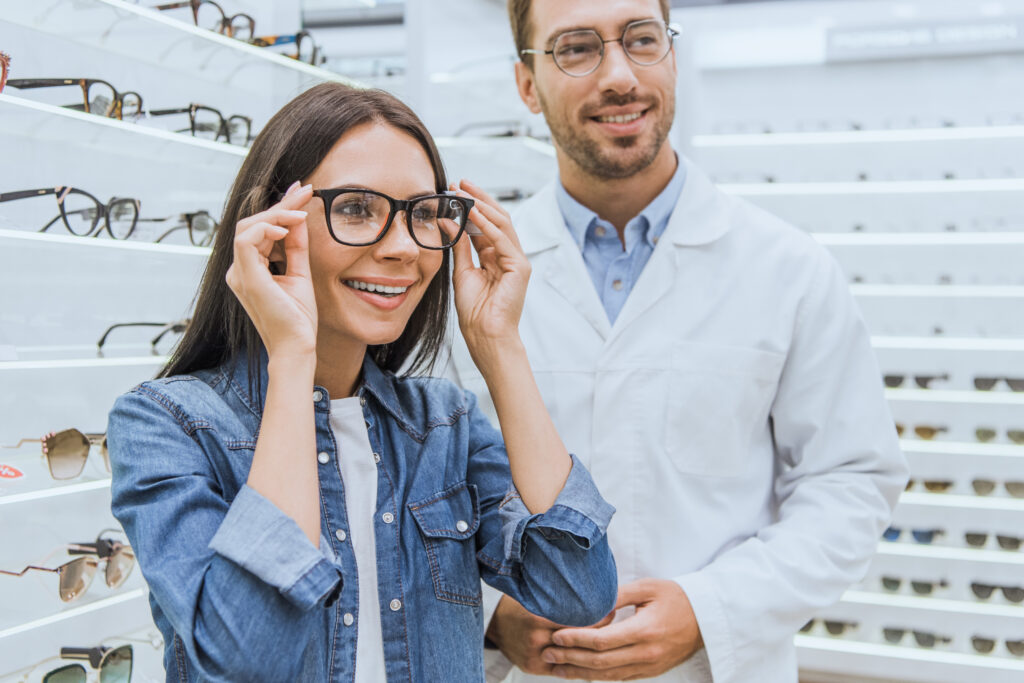 woman choosing eyeglasses while male oculist standing near in ophthalmic shop