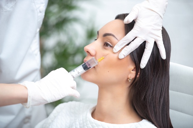 Doctor woman giving injections with a syringe injects around the eyes.