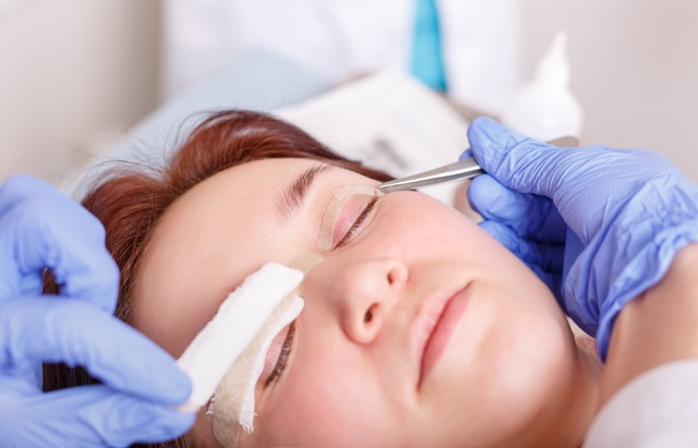 Surgeon applies a bandage to the female patient's eyelids after a blepharoplasty operation.