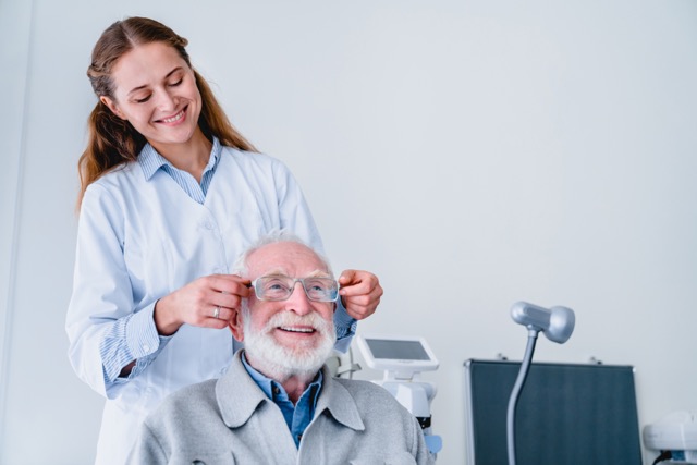 Oculist helping an elderly man try on glasses