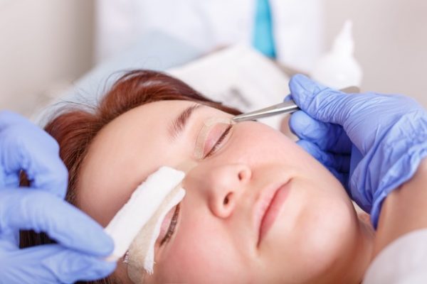 Surgeon applies a bandage to the female patient's eyelids after a blepharoplasty operation.